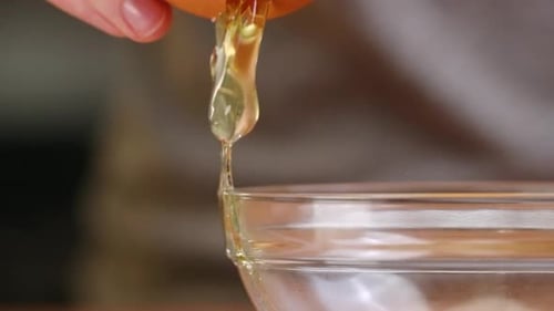 Braunes Ei wird an der Seite einer Rührschüssel aus klarem Glas geknackt und auseinandergezogen, während Eigelb und Weiß
