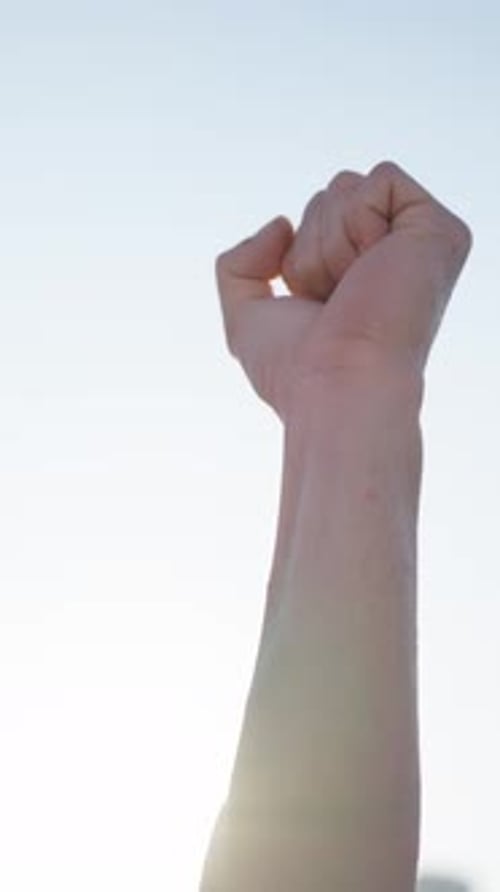 Arm Raising Clenched Fist Against Bright Sky