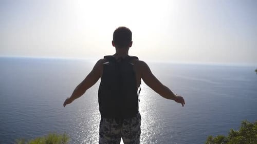 Unrecognizable Hiker with Backpack Standing on Edge of Mountain and Victoriously Raising Hands Male