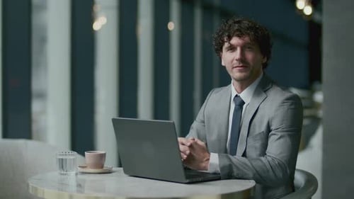 Portrait of Smiling Businessman Sitting at Cafe Table with Laptop and Coffee