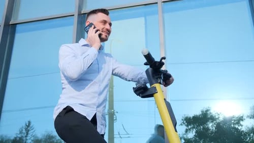 Young Office Manager Talking on the Phone Using an Electric Scooter Businessman is Working