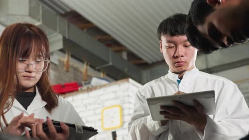 Inventor in Lab Coat Taking Notes on Tablet in Mechanical Workshop