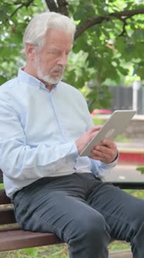 Senior Old Man using Tablet while Sitting Outdoor on a Bench, vertical video