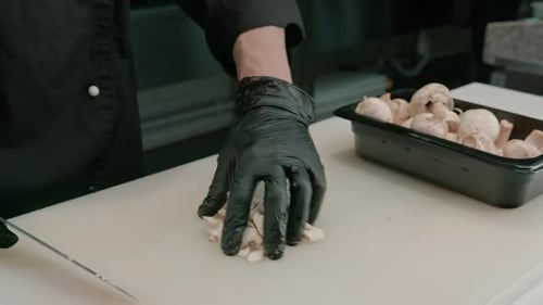 Close-up of a sushi maker in gloves cutting a mushroom on a white board in a professional kitchen