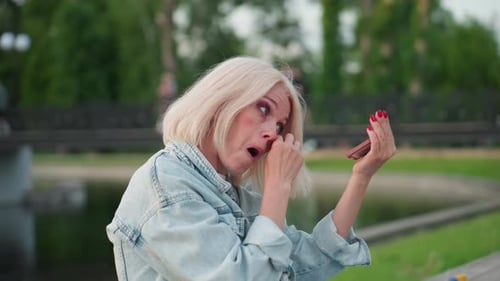Mature Woman Adjusts Makeup and Cleans Paint Smudges with Compact Mirror Outdoors