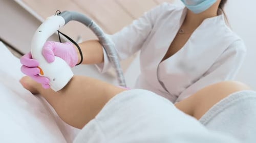 Cosmetologist Performs Laser Hair Removal of the Patient's Legs in a Modern Cosmetology Clinic