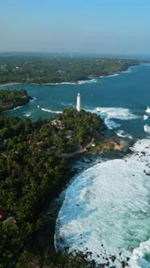 Drone View of Historic Beacon Lighthouse Towering Above Palm Trees Flanked By Turquoise Water