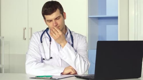 Exhausted Male Doctor Takes a Moment to Relieve Stress at the Office