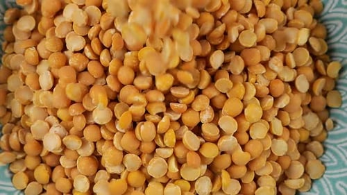 Dried peas are poured into a blue ceramic bowl. Top view. Slow motion.