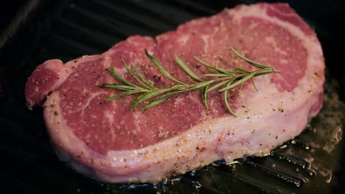 Close up of steak cooking on a grill pan topped with fresh rosemary