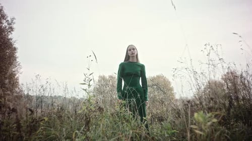 Model gracefully posing in a flowing green dress amidst a serene field setting