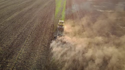 Drone Sliding Shot of Tractor Cuts Furrows in Farm Field for Sowing Farm Tractor with Rotary Harrow