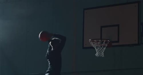 Cinematic slow motion shot of an young professional male player is making a slam dunk during a bas