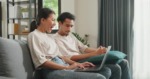 Couple Using Laptop Computer Sitting on Couch Indoors