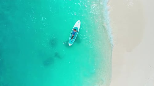 Ein kleines Mädchen liegt auf einem SUP-Board in türkisfarbenem Wasser mit weißem Sandstrand mit Stachelrochen und