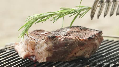 I place a sprig of rosemary on the beef steak, which is sizzling on the grill grate, capturing a clo