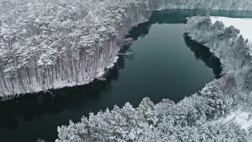 Flying above snowy forest and small river in winter, Poland.