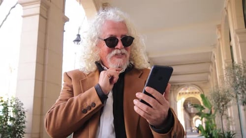 Smiling Man Uses Smartphone Outdoors in City Arcade