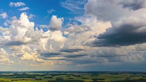 A large panoramic sky with impressive cumulus clouds over a green rural landscape