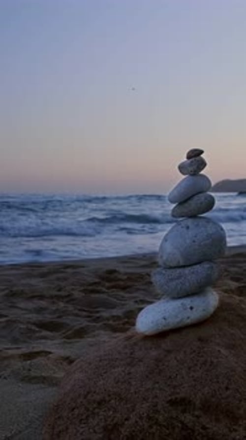 Balance stones stack on beach at sunset. Rock and sea waves in background.