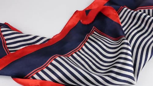 A light silk scarf in blue, white and red stripes slowly falls in soft folds on a white background.