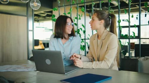 In a Modern Office Two Women Collaborate Brainstorm and Work Together with a Laptop They Discuss a