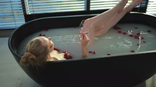 Spa Relaxation Woman Lying in Bath with Holding Glass with Red Wine Girl Relaxing in Bathroom at
