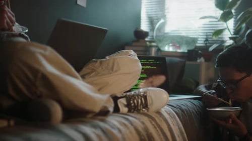 Two Young Adults Using Laptops and Eating