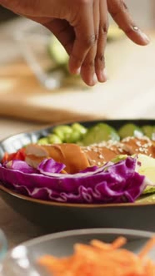 Vertical video: Entering hand adding seeds over poke bowl on counter, placing sauce cup, finishing