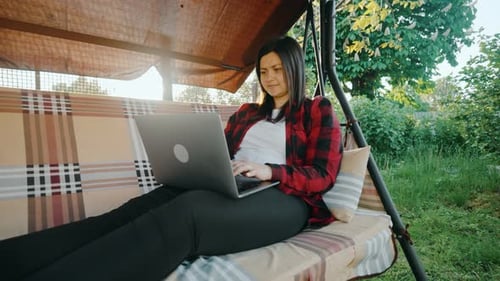 Woman Relaxes on Porch Swing with Laptop