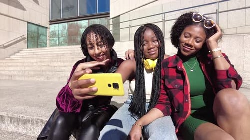 Low angle view of three multi-ethnic friends smiling while sharing a mobile outdoors