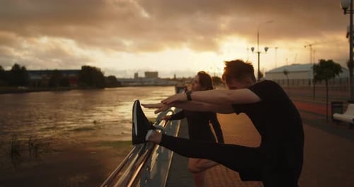 Young Man and Woman Training on the Embankment Near the Stadium at Sunset