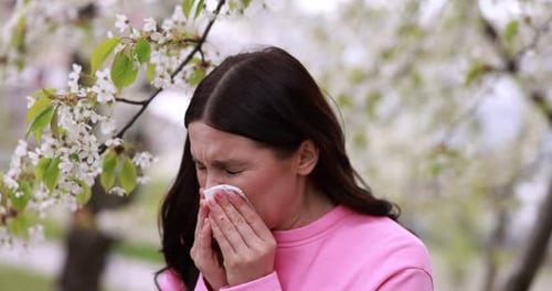Seasonal allergy. Woman sneezing in park on spring day