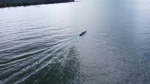 View of a fishing boat sailing on the coast with mountains and clouds in the background
