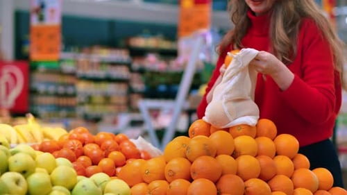 Mujer recogiendo naranjas en una bolsa reutilizable en una tienda. Temáticas del Día de la Tierra y la Ecología