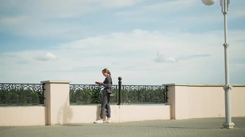 Lady in Grey Clothing Reading Book Near Fence with Scenic Nature View