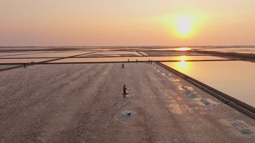 Aerial capture of Thai salt farmers at sunset in seawater fields