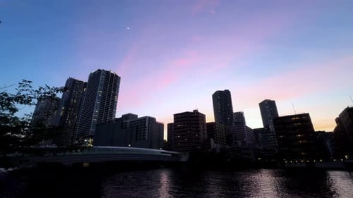 City skyline at sunset with colorful sky reflecting on a calm river