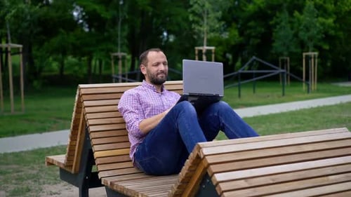 Young Man Sitting with Laptop on Bench in the Park 30s
