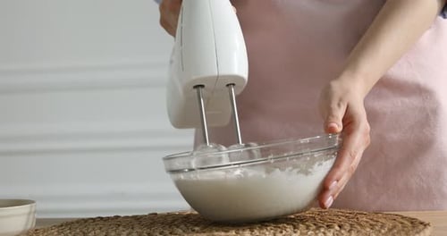 Woman whisking cream with hand mixer at table indoors, closeup. Space for text