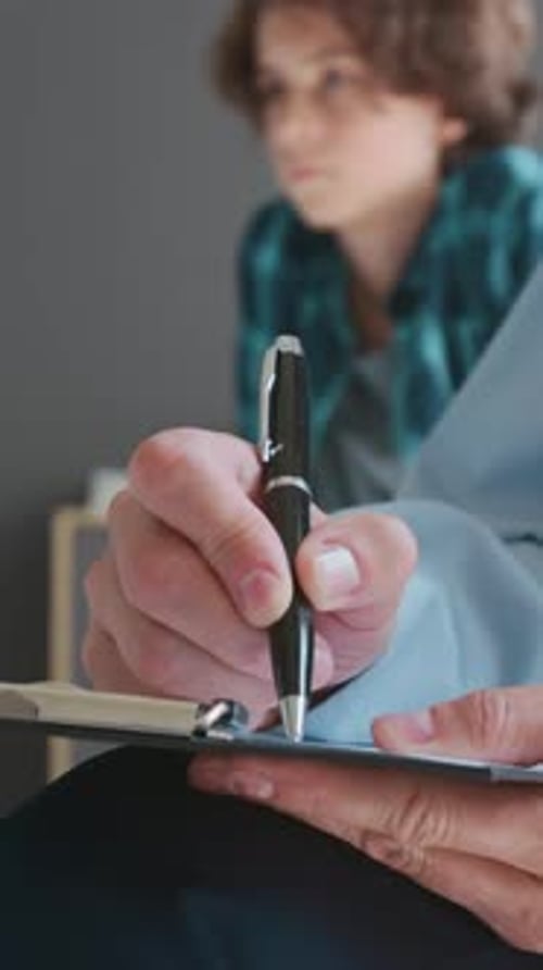 Close-up of Unrecognizable Counselor Writing Down Notes at School Therapy