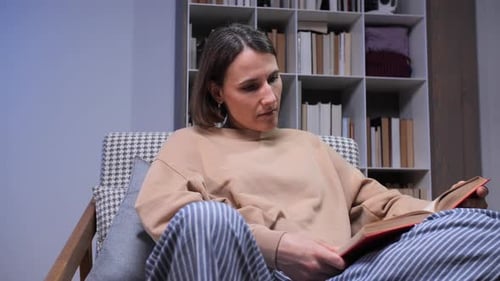 Frau genießt einen ruhigen Moment und sitzt bequem in einem Sessel mit einem klassischen Buch in der Hand