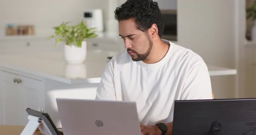 Hombre afroamericano con camiseta blanca trabajando en una computadora portátil plateada, viendo un monitor negro después de la alerta