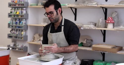 Geschickter Handwerker, der eine Schürze trägt und vorsichtig eine feuchte Tonvase auf einer sich drehenden Töpferscheibe formt, prac