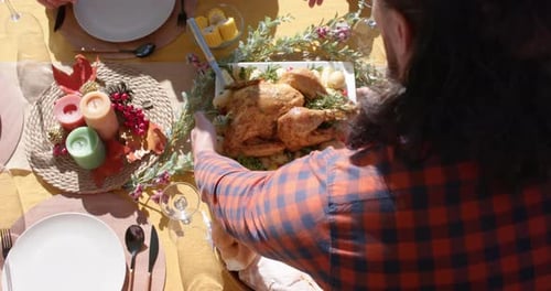 Happy diverse male and female friends serving thanksgiving celebration meal in sunny garden