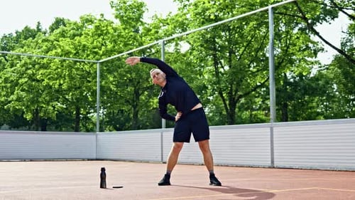 Man Stretching on Sports Court Near Green Trees