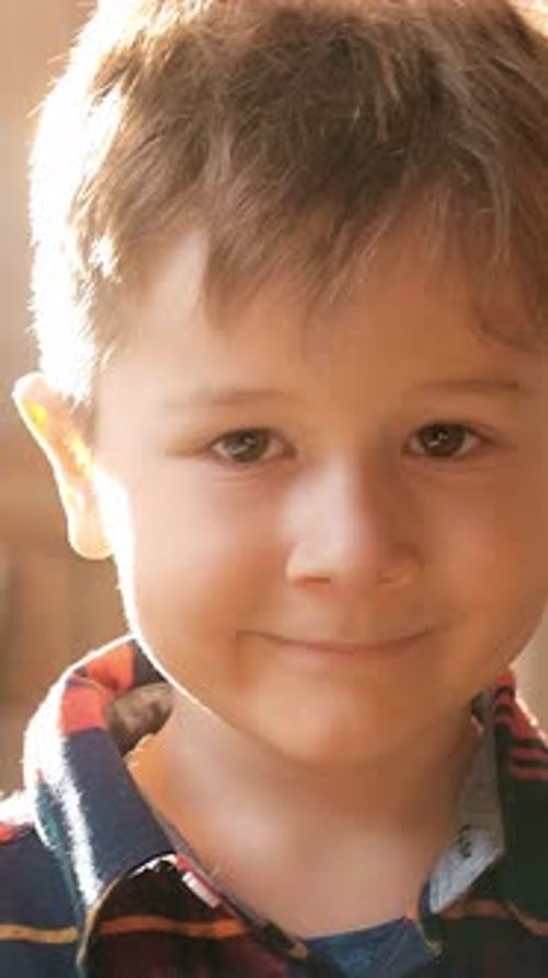 Un jeune garçon à l'expression ludique sourit chaleureusement, montrant son innocence et sa joie dans un endroit doucement éclairé