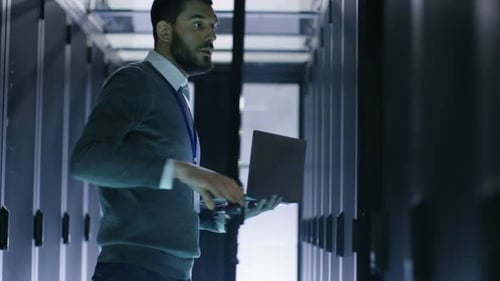 Männlicher IT-Ingenieur öffnet den Serverschrank, während er den Laptop in der Hand hält. Er arbeitet im Big Data Center