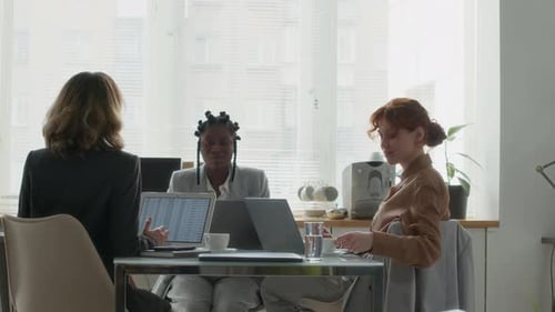 Three Young Female Colleagues Communicating during Break at Office Desk