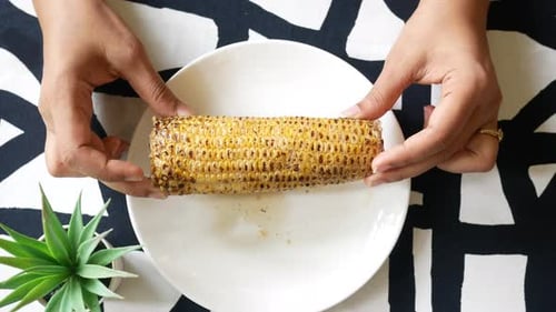Hands Hold Grilled Corn on White Plate
